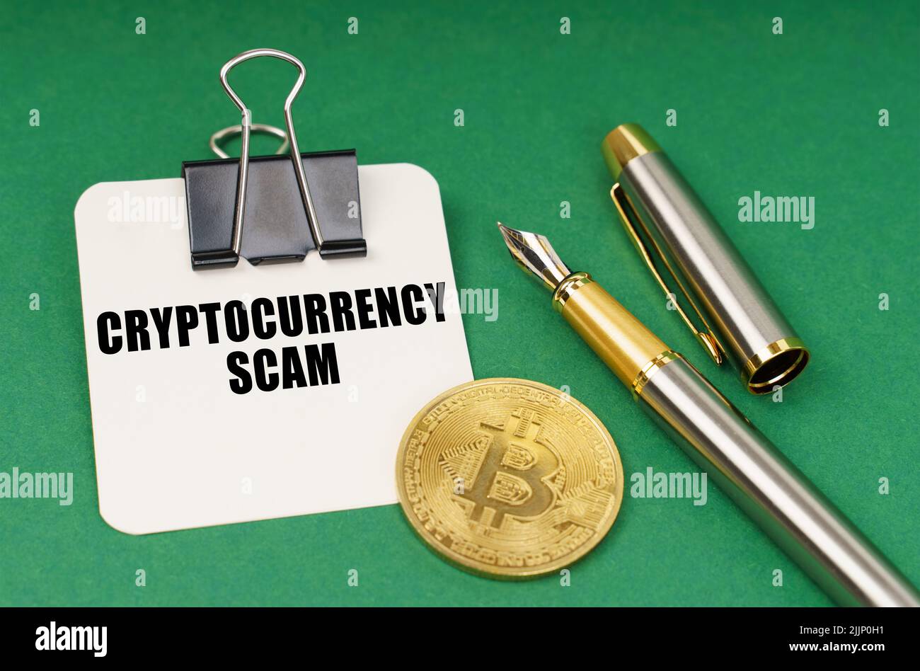 Cryptocurrency and business concept. On a green surface, a bitcoin coin, a pen and a sheet of paper with the inscription - Cryptocurrency scam Stock Photo