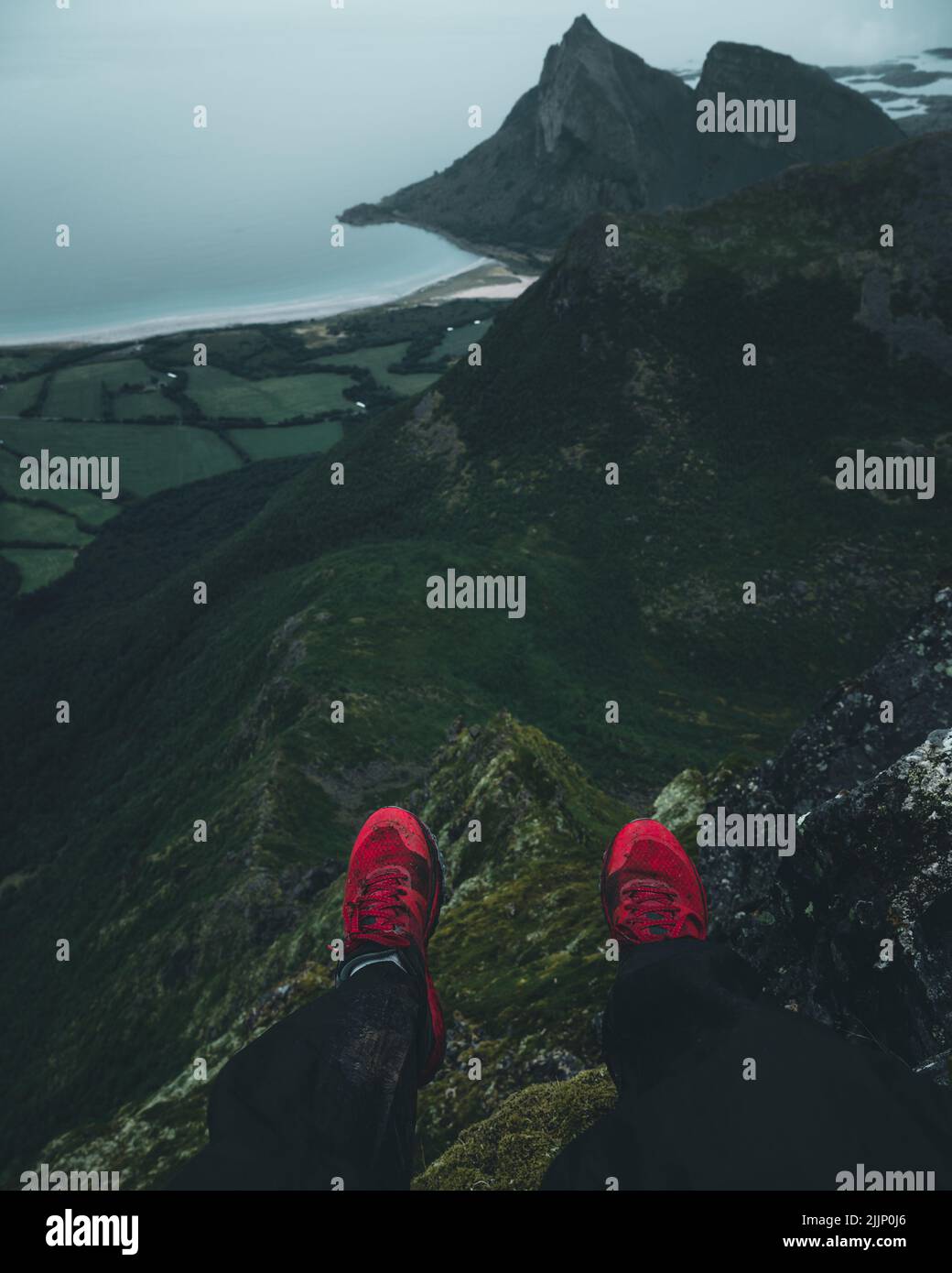 A shot of someone wearing red shoes and sitting on high point of mountain Stock Photo