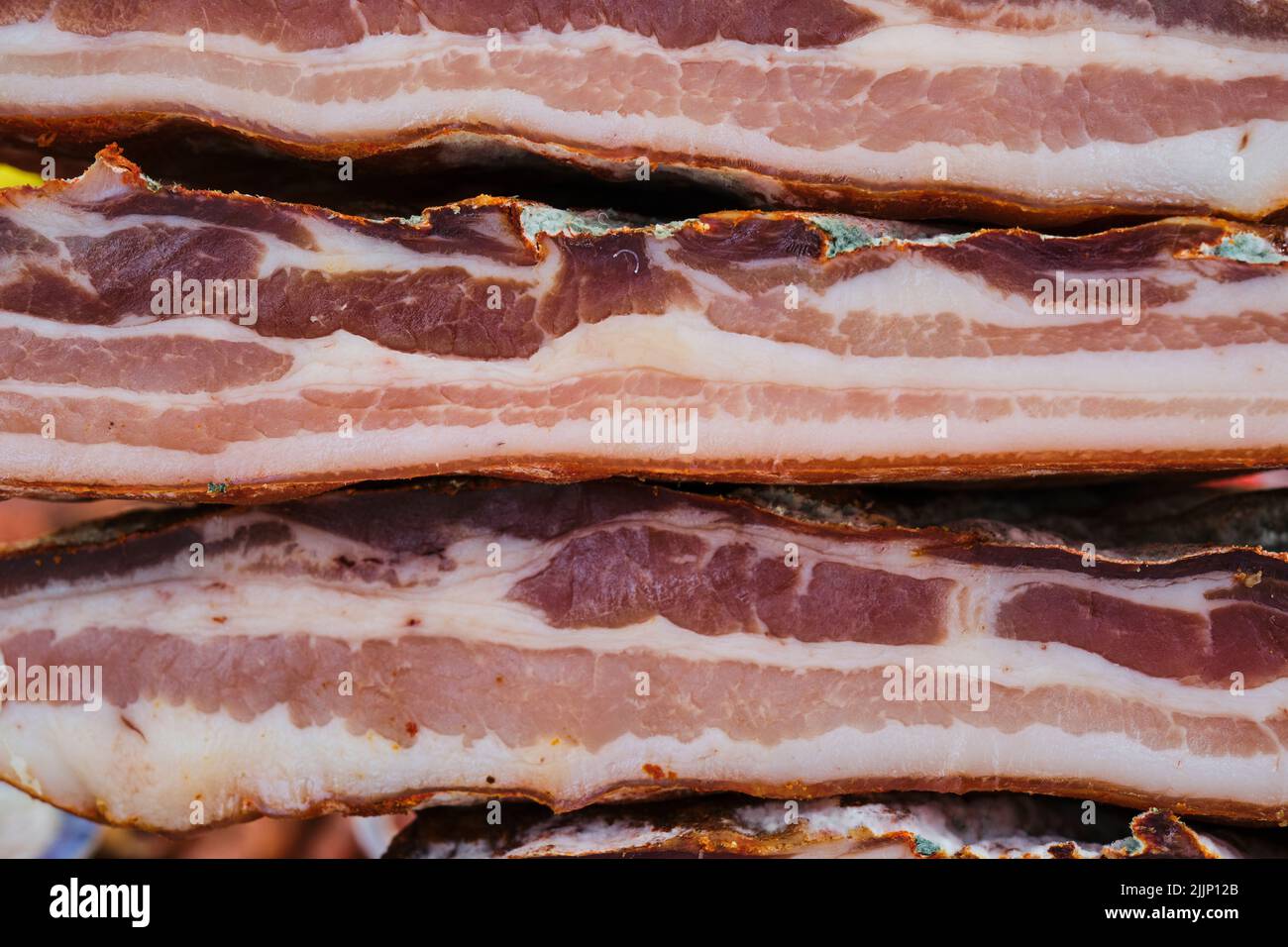 Closeup bunch of delicious cured acorn fed Iberian bacon stacked on stall on market Stock Photo