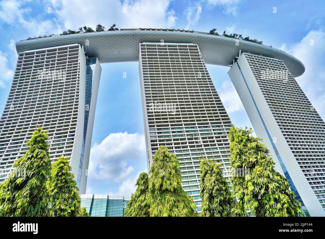 A low angle shot of the Marina Bay Sands hotel in Singapore under a cloudy sky surrounded by greenery Stock Photo