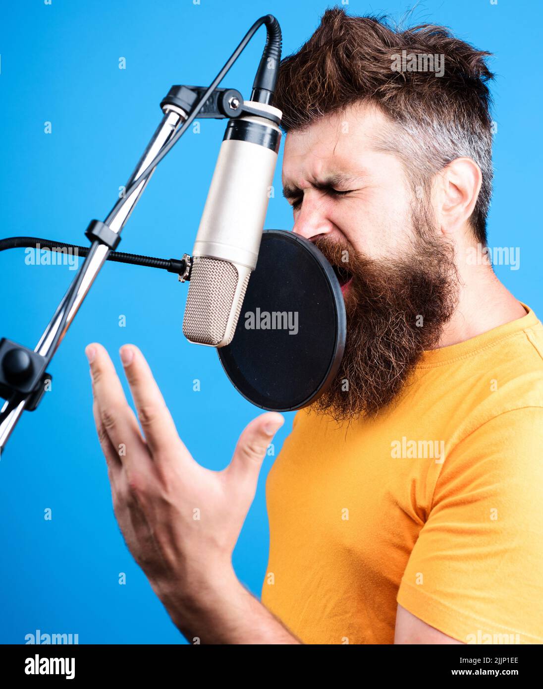 Male singer singing in condenser microphone. Professional vocalist in studio. Music, leisure concept. Stock Photo