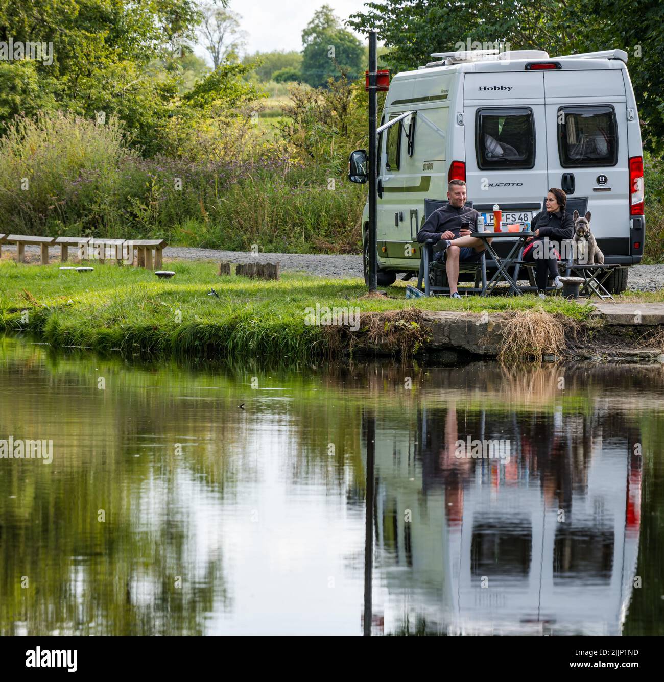 Ratho, Scotland, United Kingdom, 27th July 2022. UK Weather: sunny evening on the Union Canal. A German couple enjoy an evening camping site with their camper van and dog beside the canal Stock Photo
