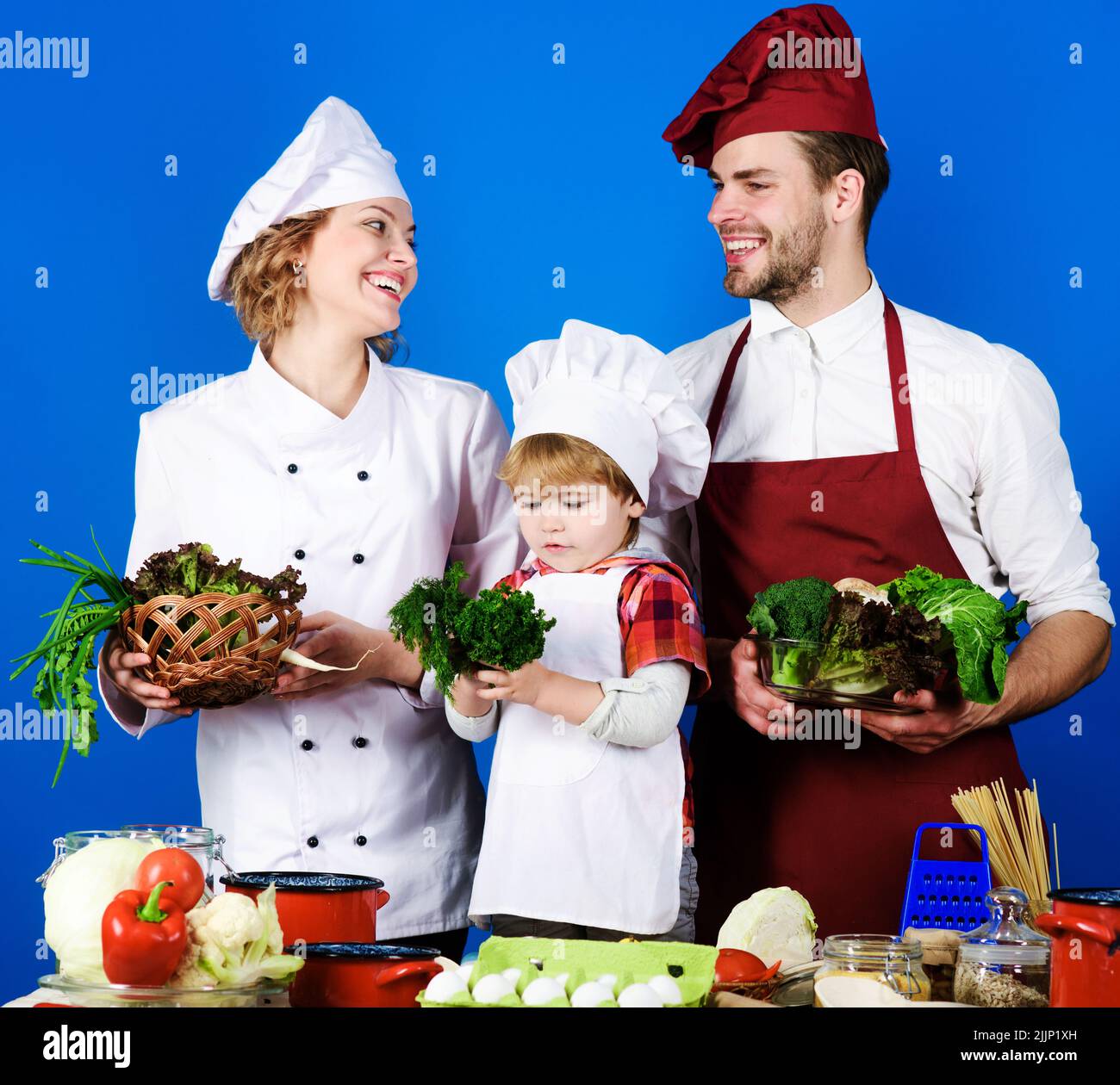 Cooking. Happy family preparing dinner together at kitchen. Parents teaching little son how to cook. Stock Photo