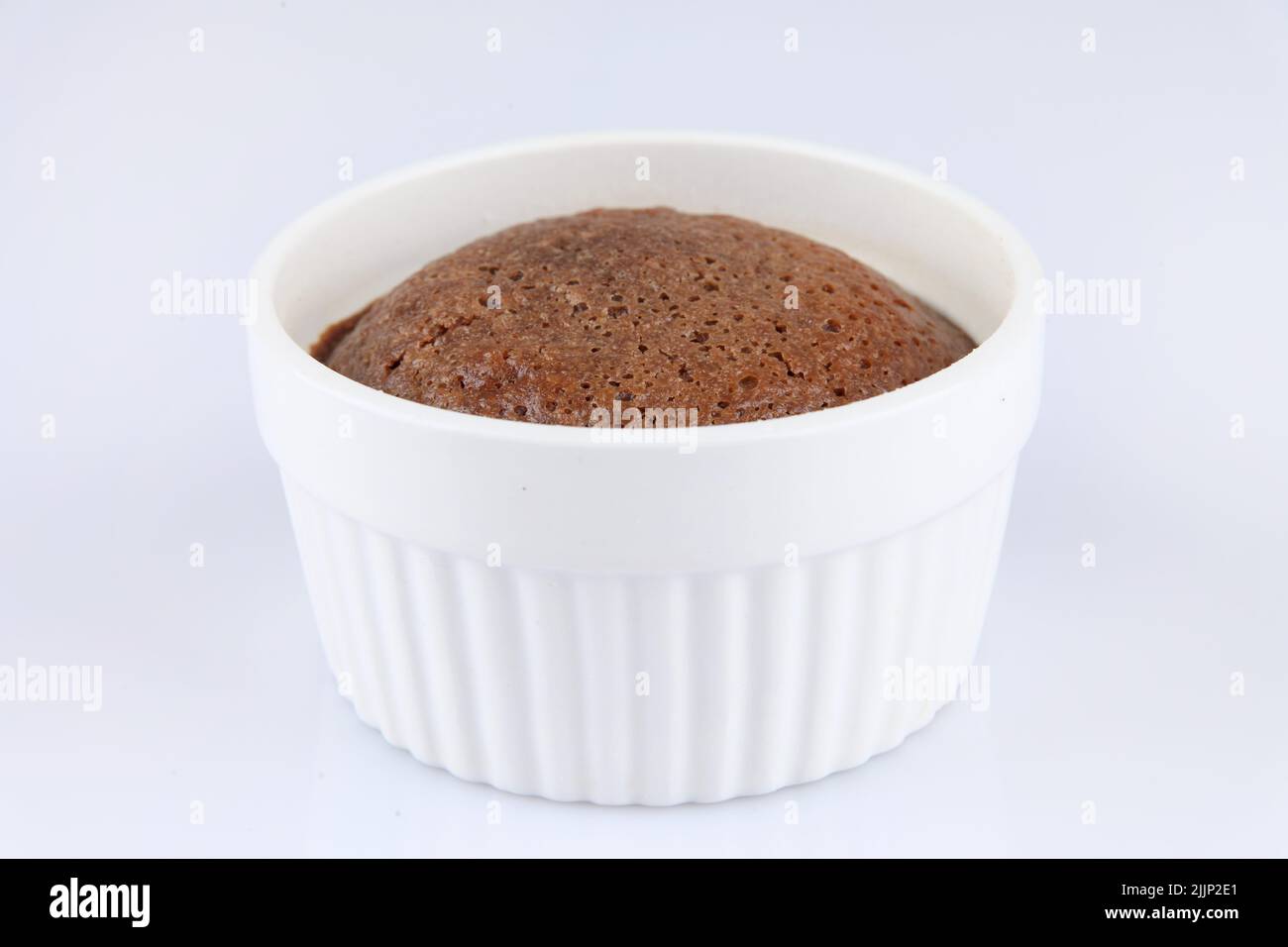 A chocolate souffle in a classic white porcelain ramekin on white