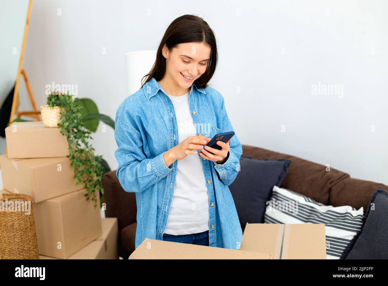 Happy young woman using mobile phone order transportation service and movers to move to new home Stock Photo