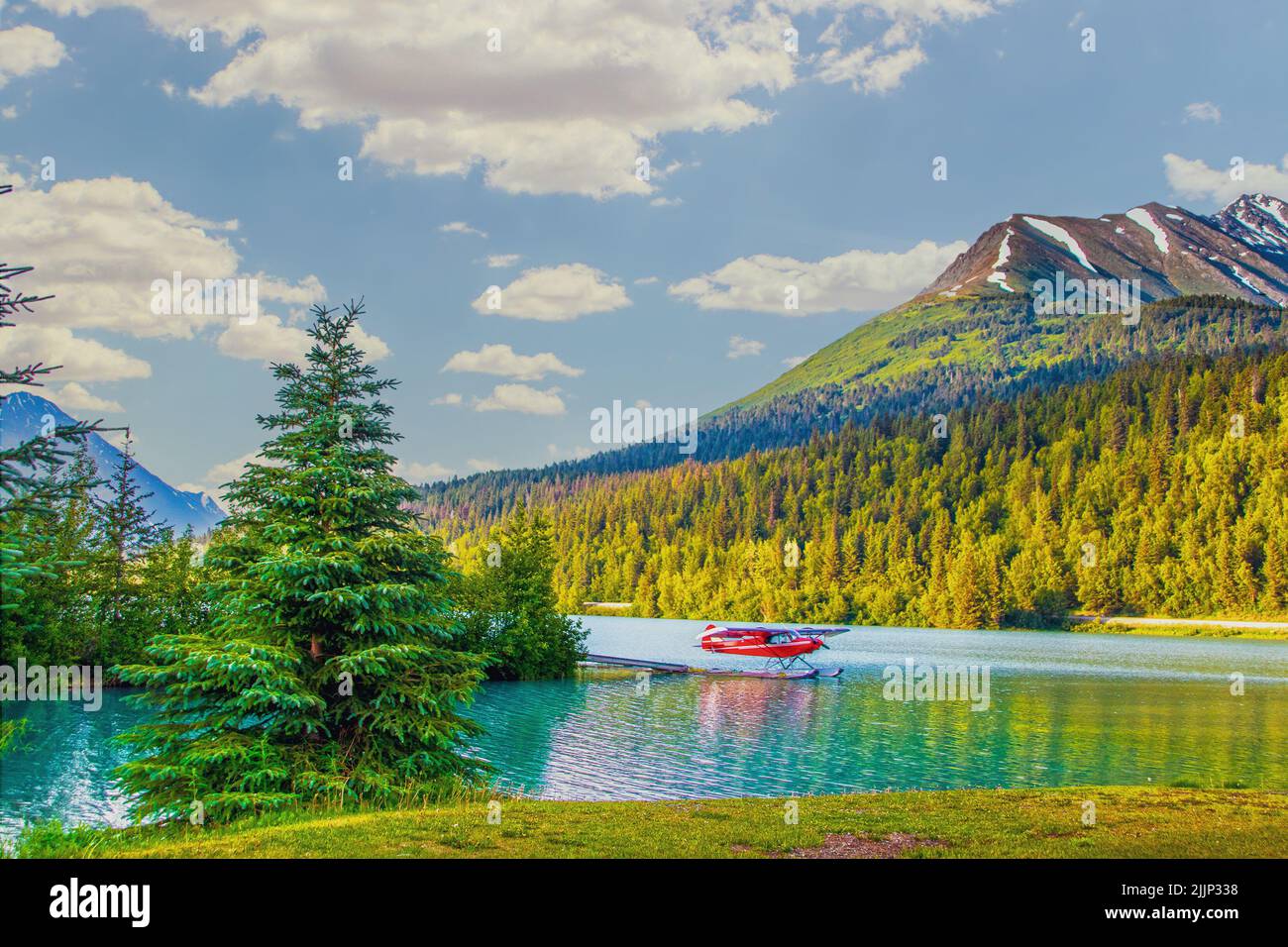 Red sea plane on lake in Moose Pass, Alaska in evening sunshine with mountains in background and surrounded by evergreen trees Stock Photo