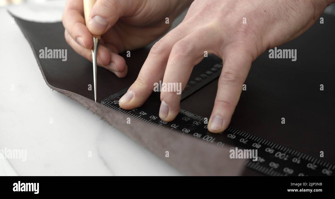 Leather craftsman working with natural leather work with awl and metal