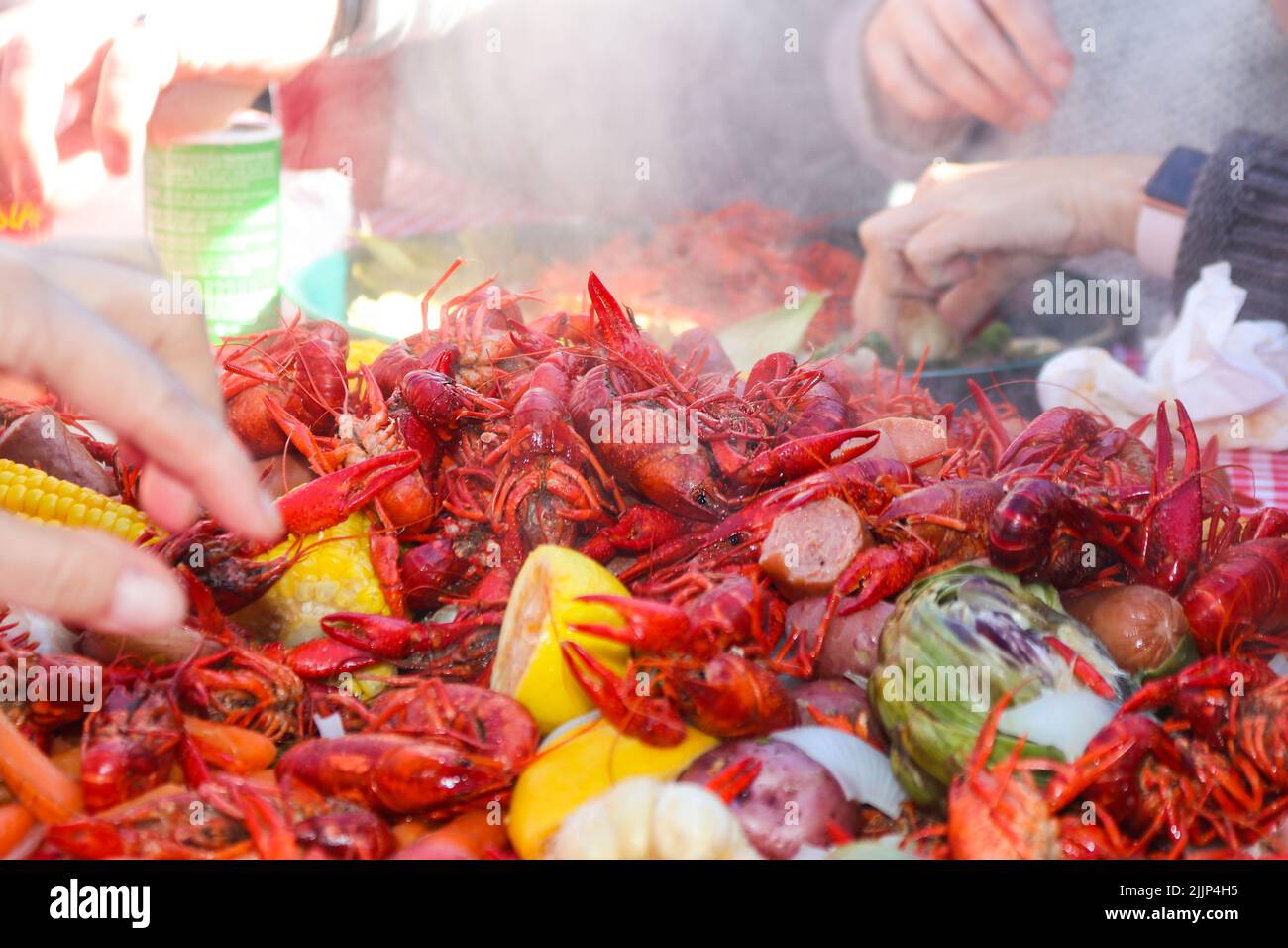 Steaming crayfish and lemons and sausages and artichokes and other vegestables piled on table with multiple hands reaching in to retreive food - selec Stock Photo