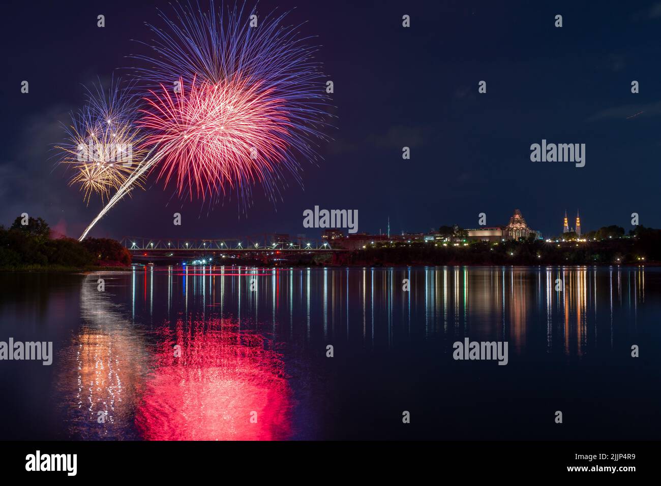 A beautiful view of fireworks in the night sky over the lake by the city Stock Photo