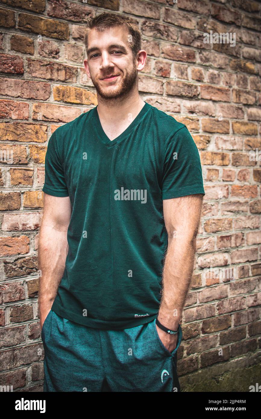 A vertical shot of a young Caucasian male standing against a brick wall Stock Photo