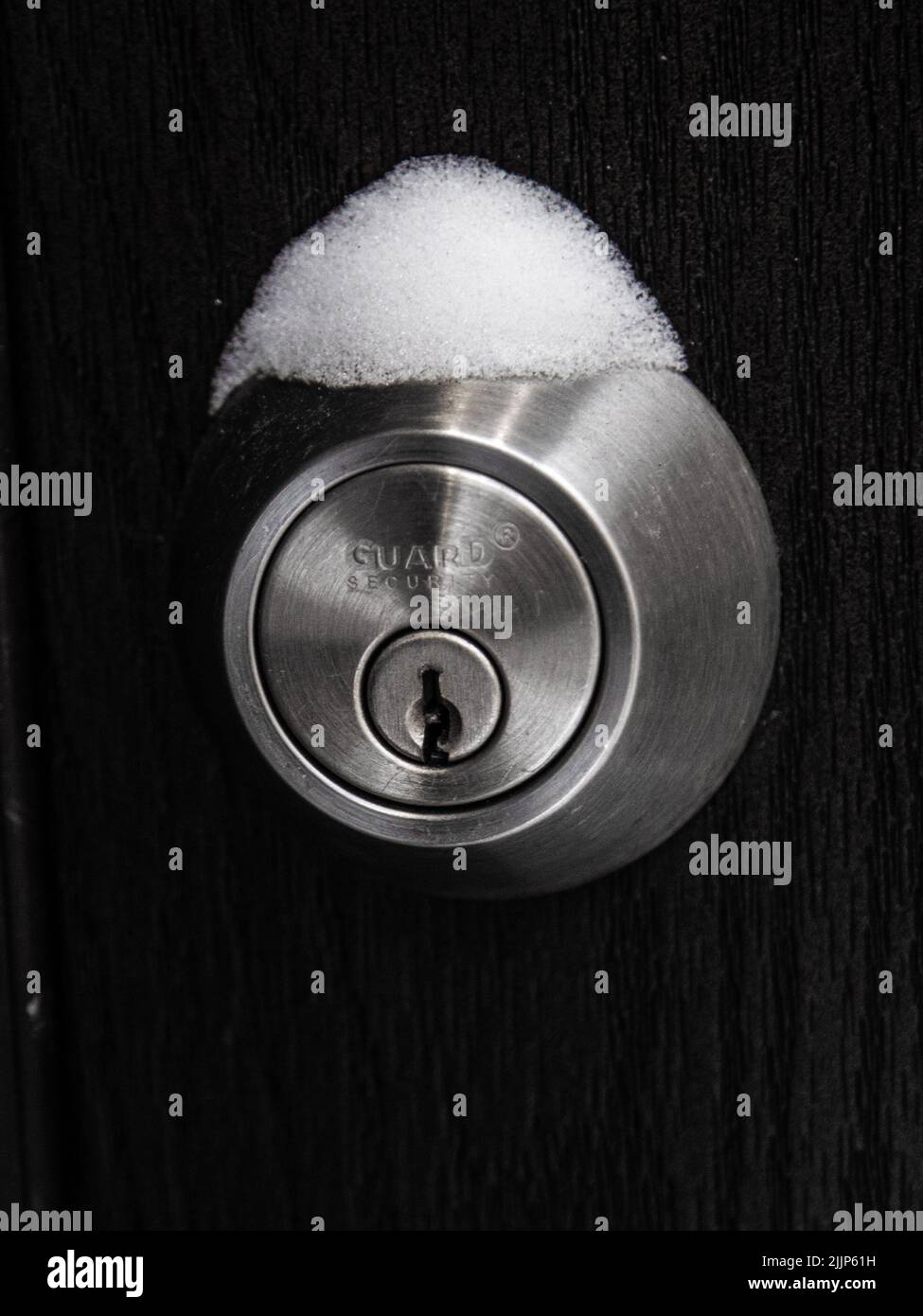 A vertical shot of snow covering the door lock against the wooden background Stock Photo