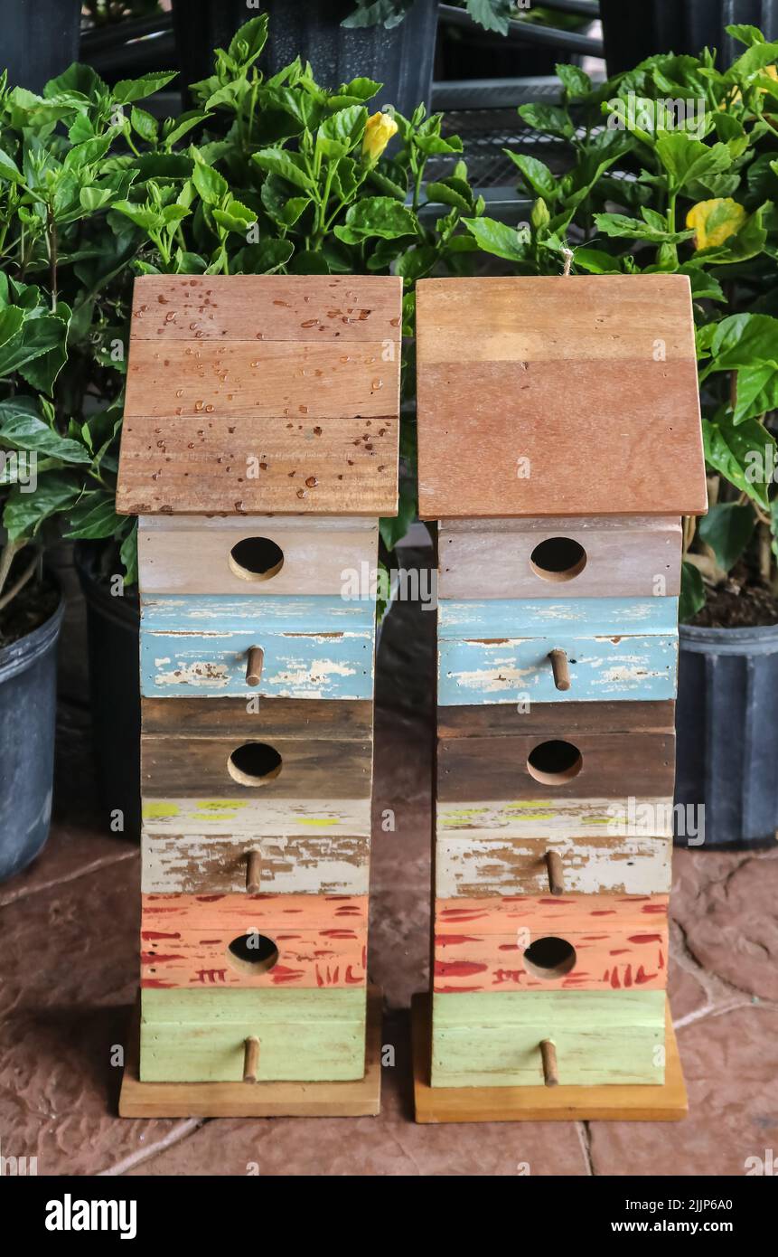 Two multi-story homemade-looking birdhouses for sale beside potted hibiscus plants in the springtime Stock Photo