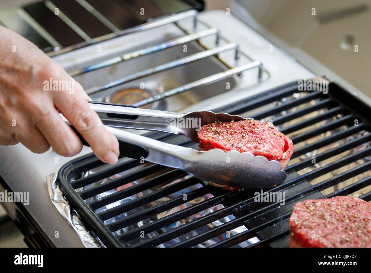Using tongs to place bacon wrapped filet mignon steak on outdoor