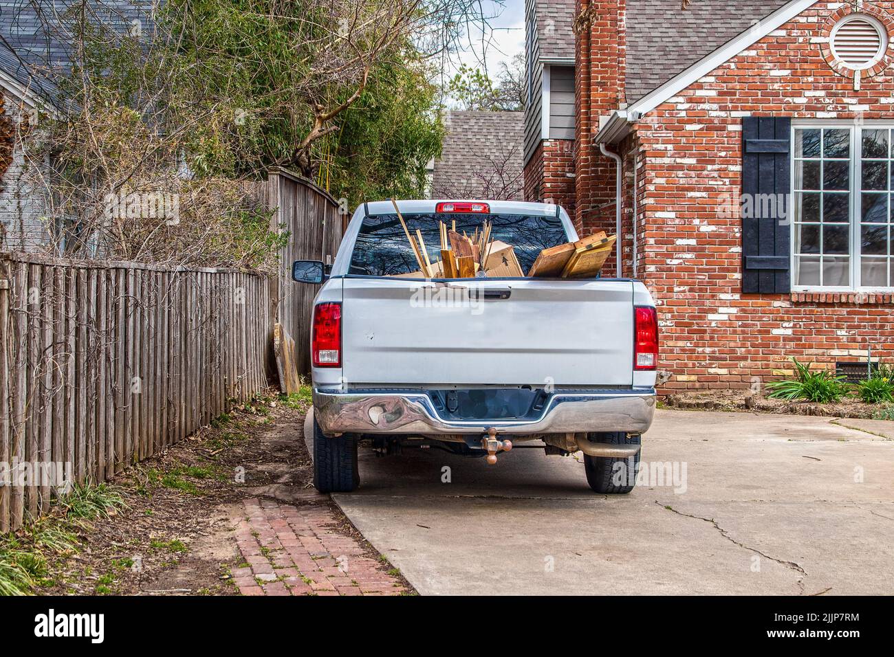 White pickup truck full of trash-boards and boxes- parked in driveway of brick house by security fence - ready to haul it away Stock Photo