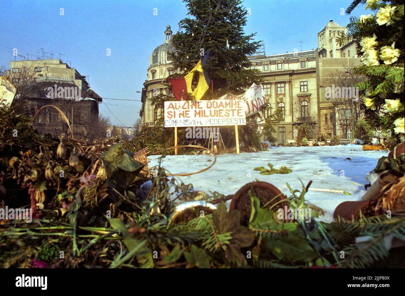 Bucharest, Romania, January 1990. Memorial for the victims of the Romanian anticommunist revolution of December 1989 in the University Square, one of the key points in the uprising.  Romanian flag with the Socialist emblem cut, an anti-communist symbol during the Romanian Revolution of 1989. Sign saying 'Hear us, Lord and have mercy, punish communism'. Stock Photo