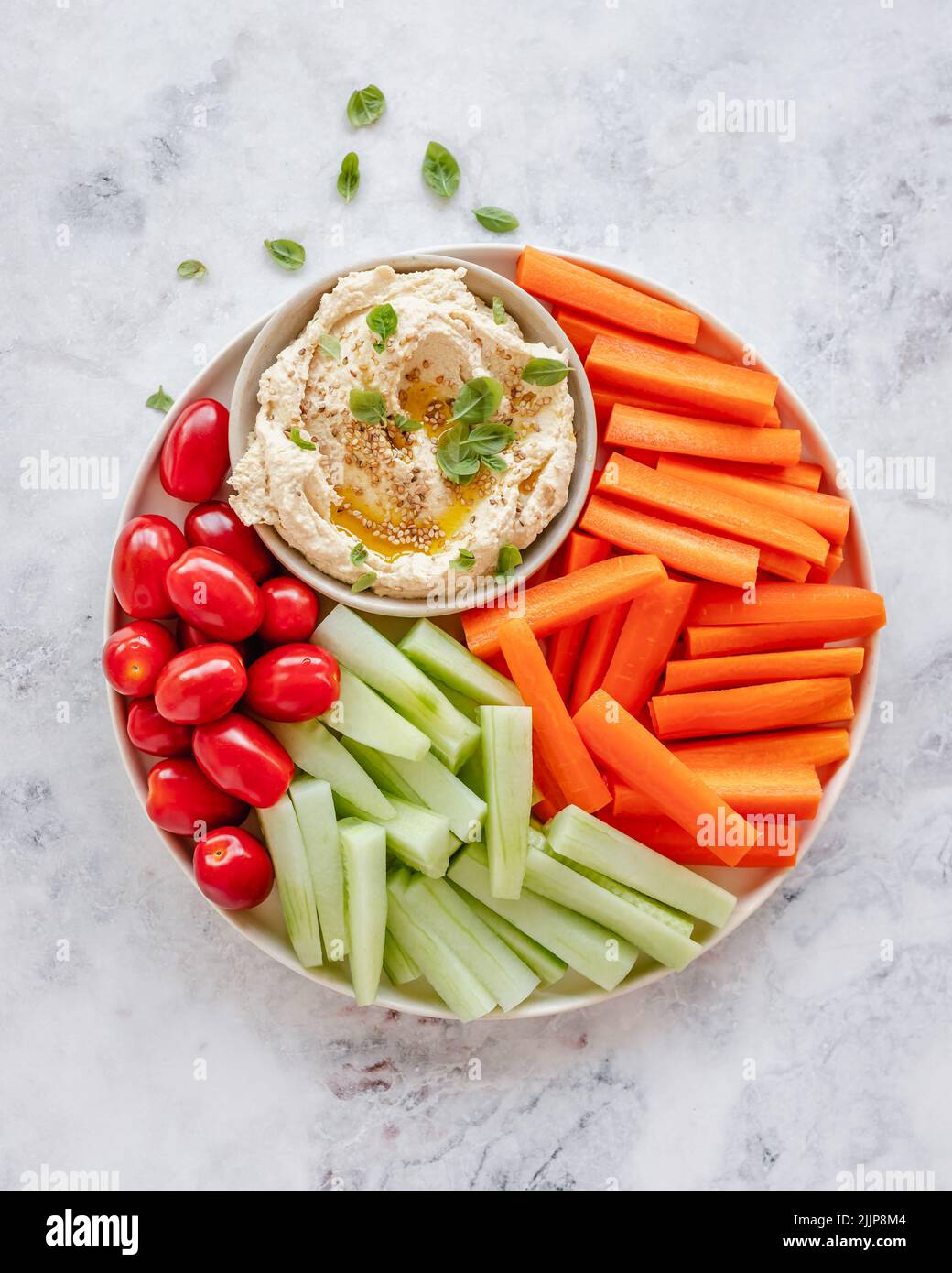 Overhead view of a bowl of hummus with cherry tomatoes, carrot and