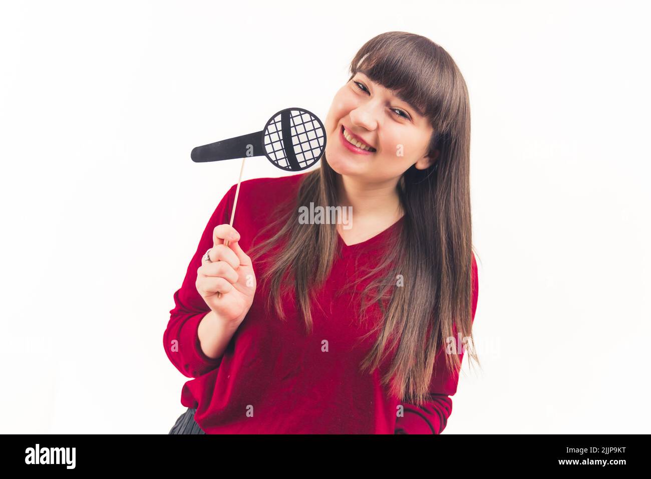 Young caucasian brunette woman with bangs smiling holding fake paper microhone. Studio shot. Isolated copy space. High quality photo Stock Photo