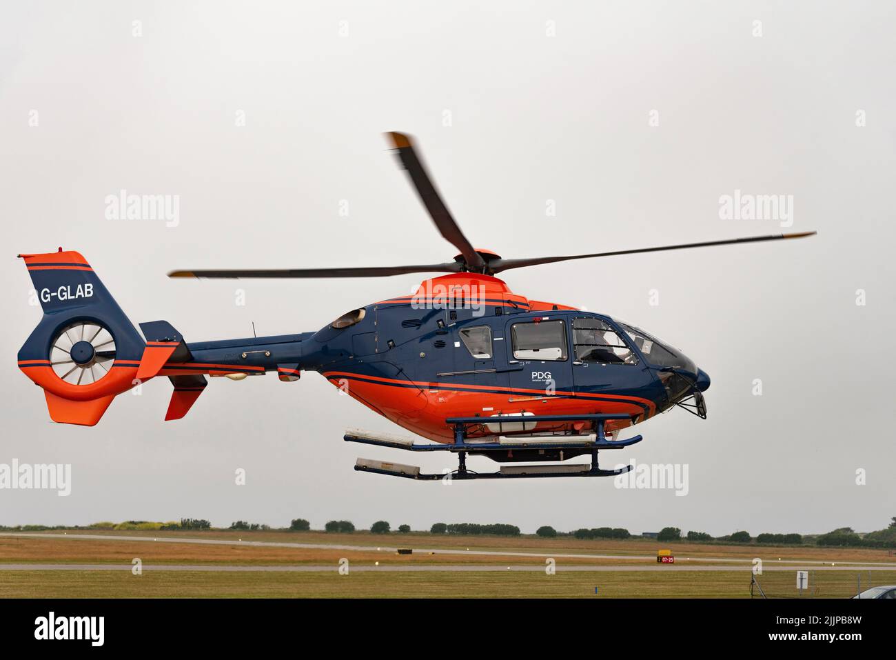 Cornwall, England, UK. 2022. A modern helicopter in flight with covered tail rotor and painted red and blue colours. Stock Photo