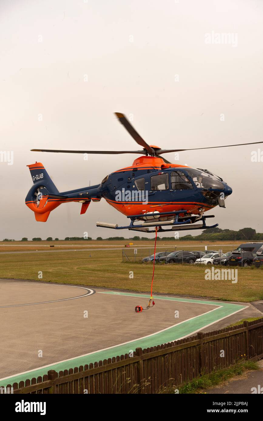 Cornwall, England, UK. 2022. Airlift helicopter with carrying strap and netting cargo carrier above a Cornish airfield on a collection and delivery op Stock Photo