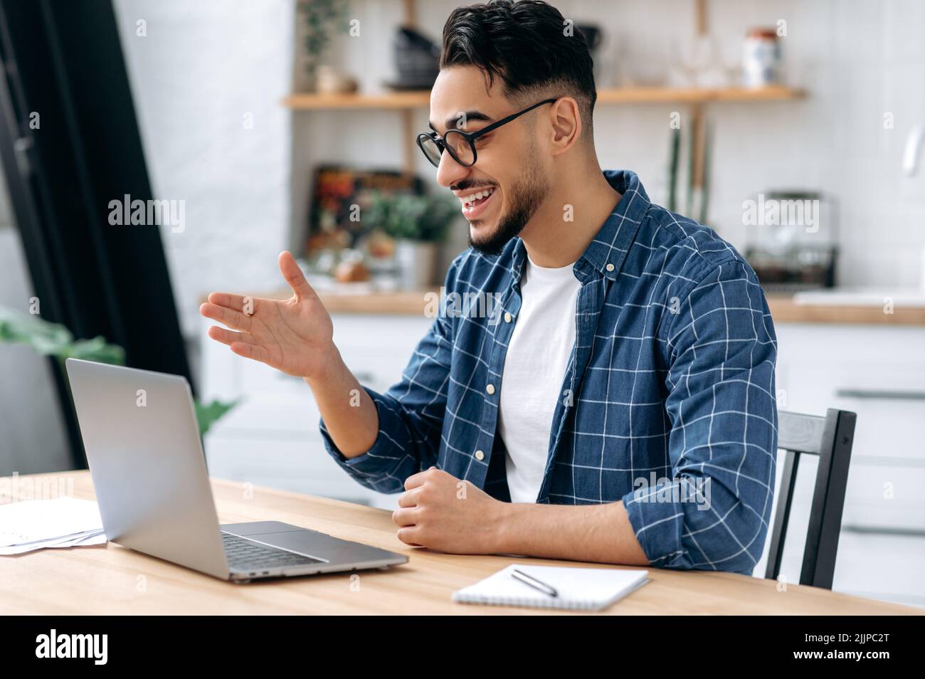 Friendly clever indian or arabian guy, freelancer, student, wearing glasses and casual stylish clothes, talking via video conference, looking at laptop, conducts virtual meeting, work from home,smile Stock Photo