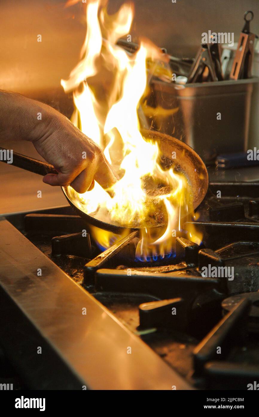 A professional chef using a pan to fry food in the kitchen with a flame
