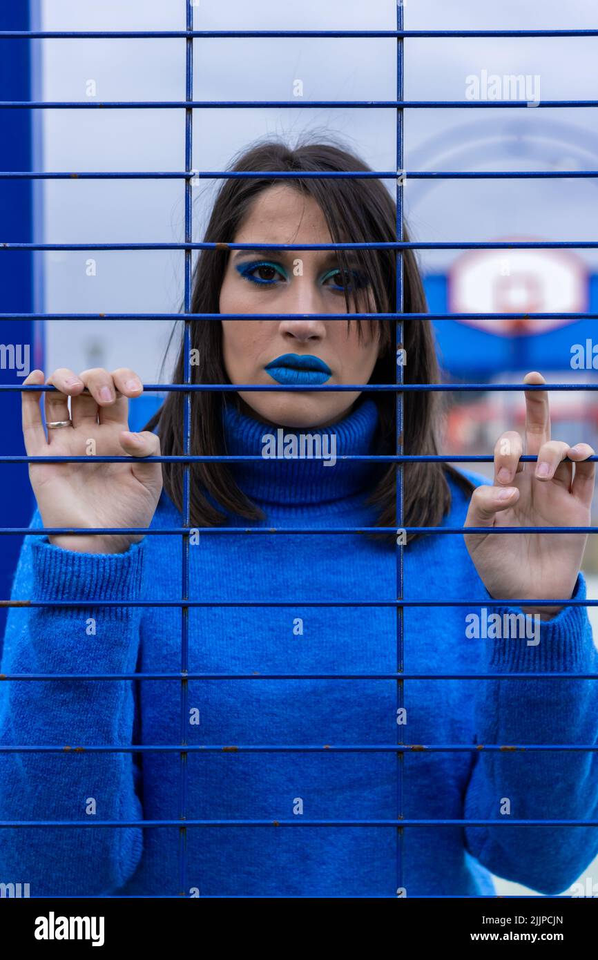 A vertical portrait of a woman dressed and made up in blue behind a prison cell. Stock Photo