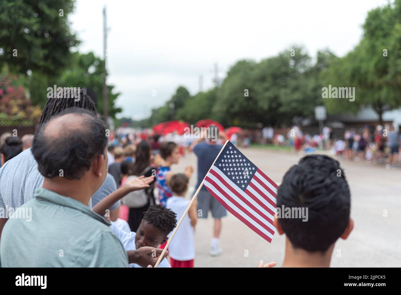 Diverse people waving American flags watching street parade on July 4th Independence Day celebration Stock Photo