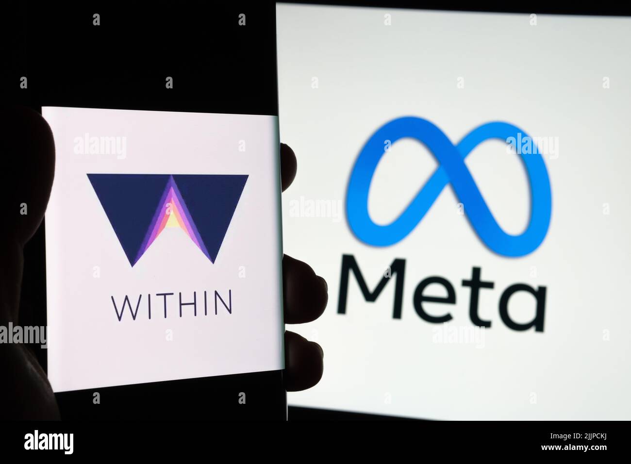 WITHIN VR app logo seen on smartphone hold in a hand and blurred Facebook Meta logo on the background. Concept for takeover. Stafford, United Kingdom, Stock Photo
