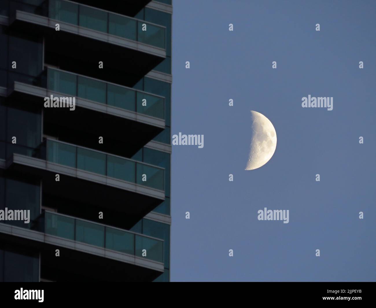 A half moon on the night sky next to modern glass building edge Stock