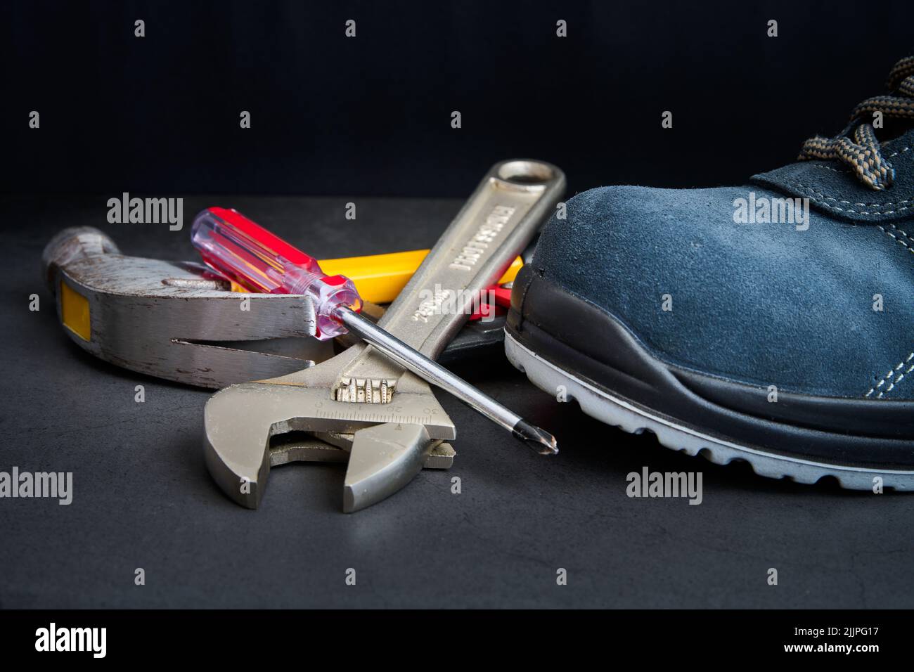 A closeup of metal tools next to a blue boot on a blurry black background Stock Photo
