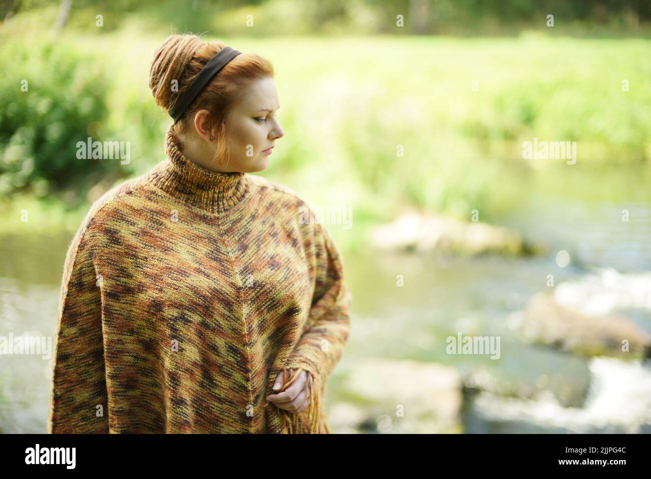 A chubby white female with ginger hair in a bun and a turtleneck posing near a river shore Stock Photo