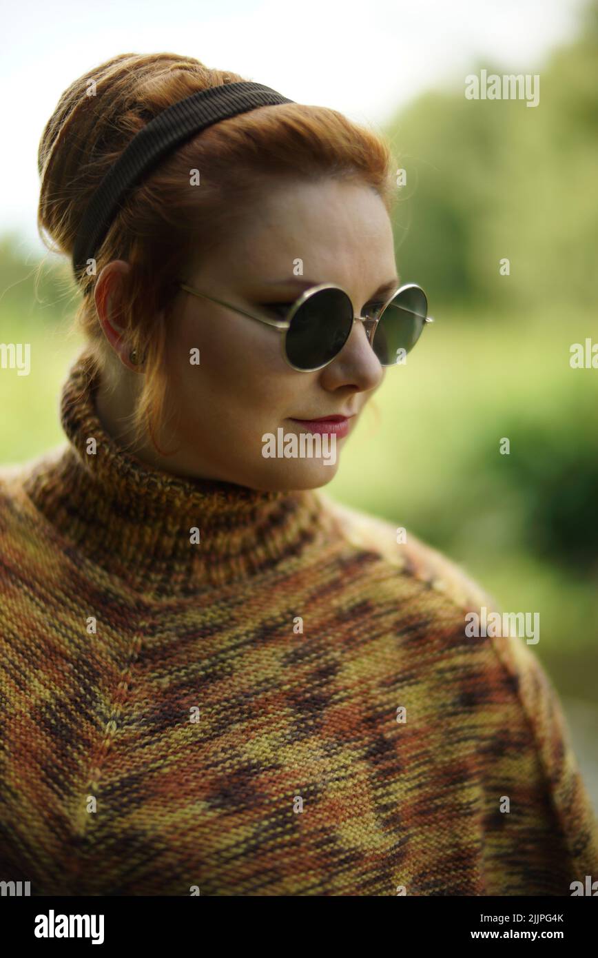 A vertical closeup shot of a female with ginger hair, round, sunglasses, and a turtleneck posing Stock Photo