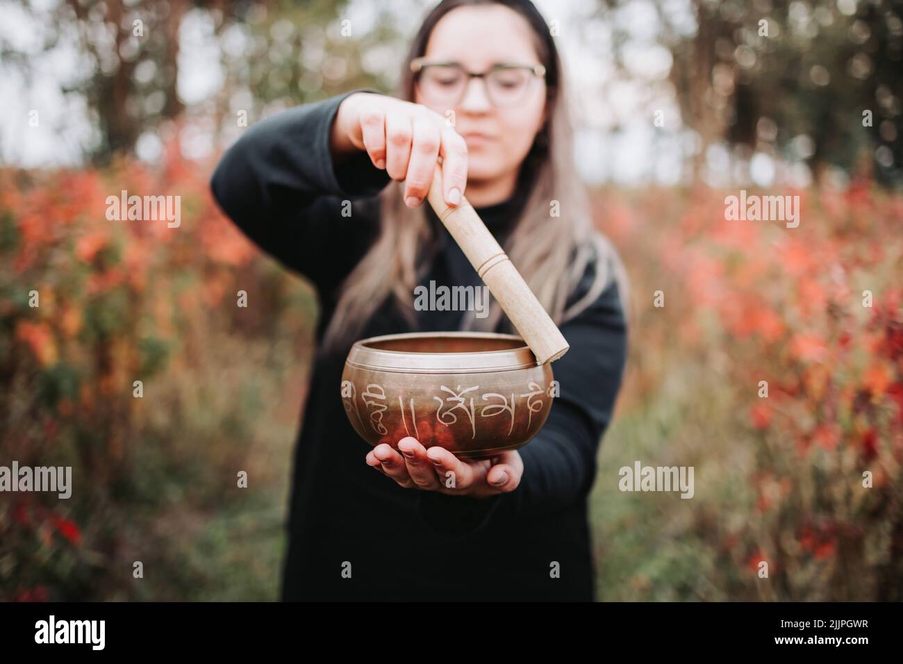 Black dressed buddhist woman holding and playing a tibetan singing bowl with a wooden stick. Selective focus Stock Photo