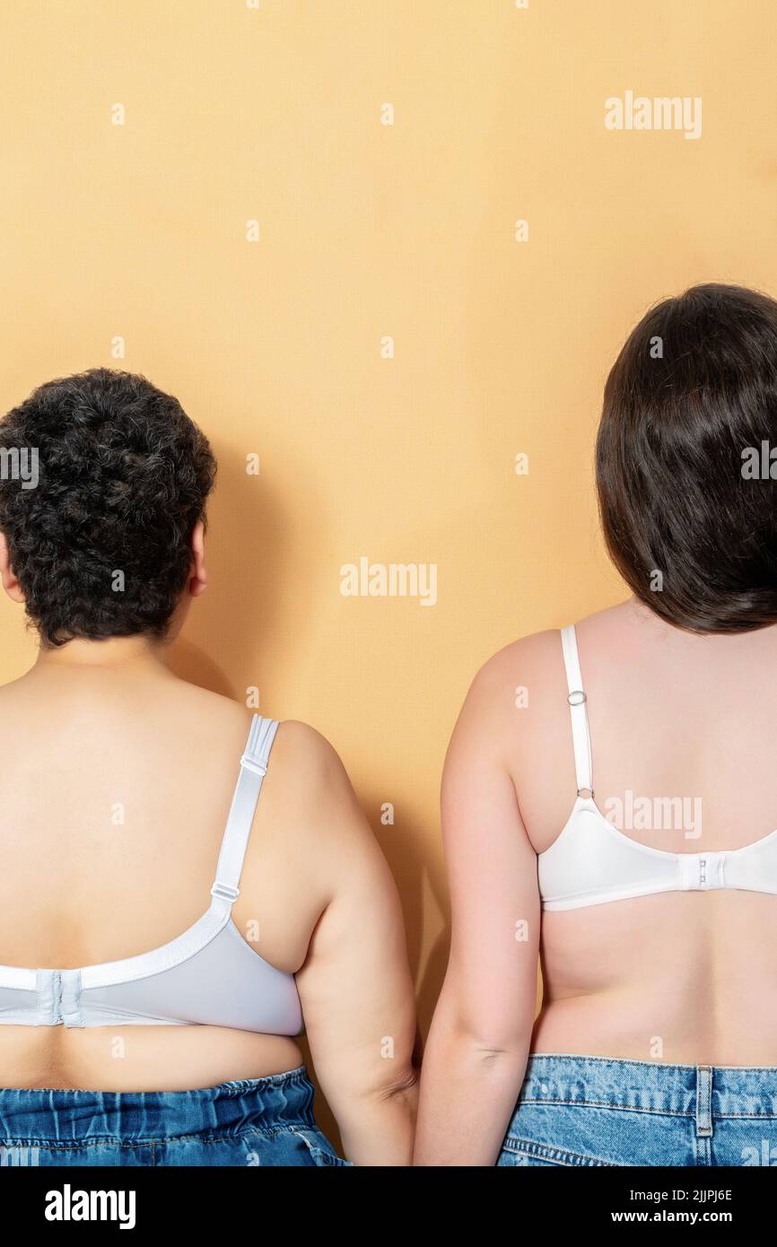 The rear view of two women with different body type posing together against yellow background - body positivity and self acceptance concept Stock Photo