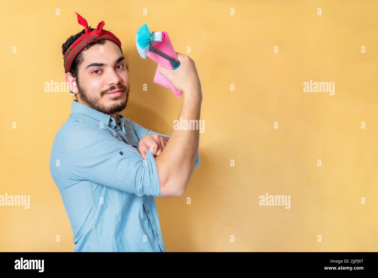 A man flexing his muscle and supporting feminism holding cloth and cleaning brush Stock Photo