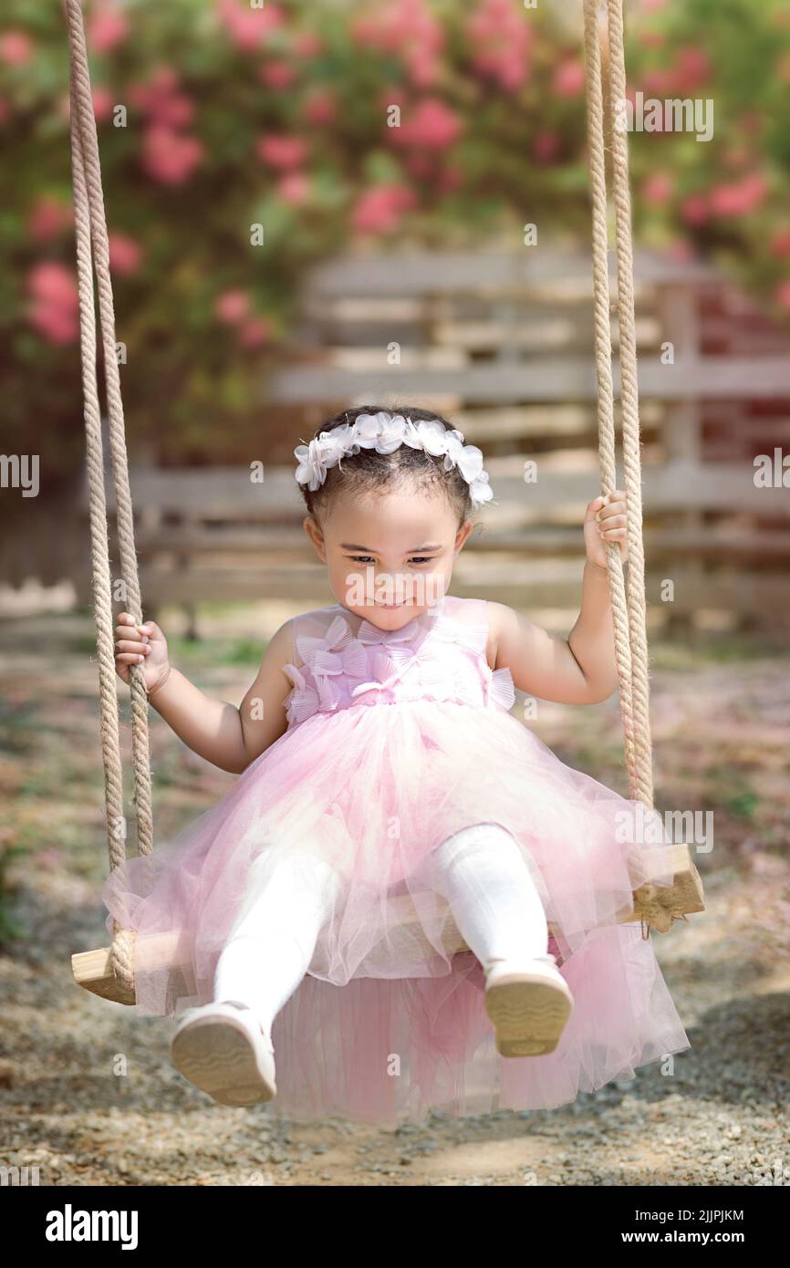 Smiling girl sitting on a swing in a garden, China Stock Photo