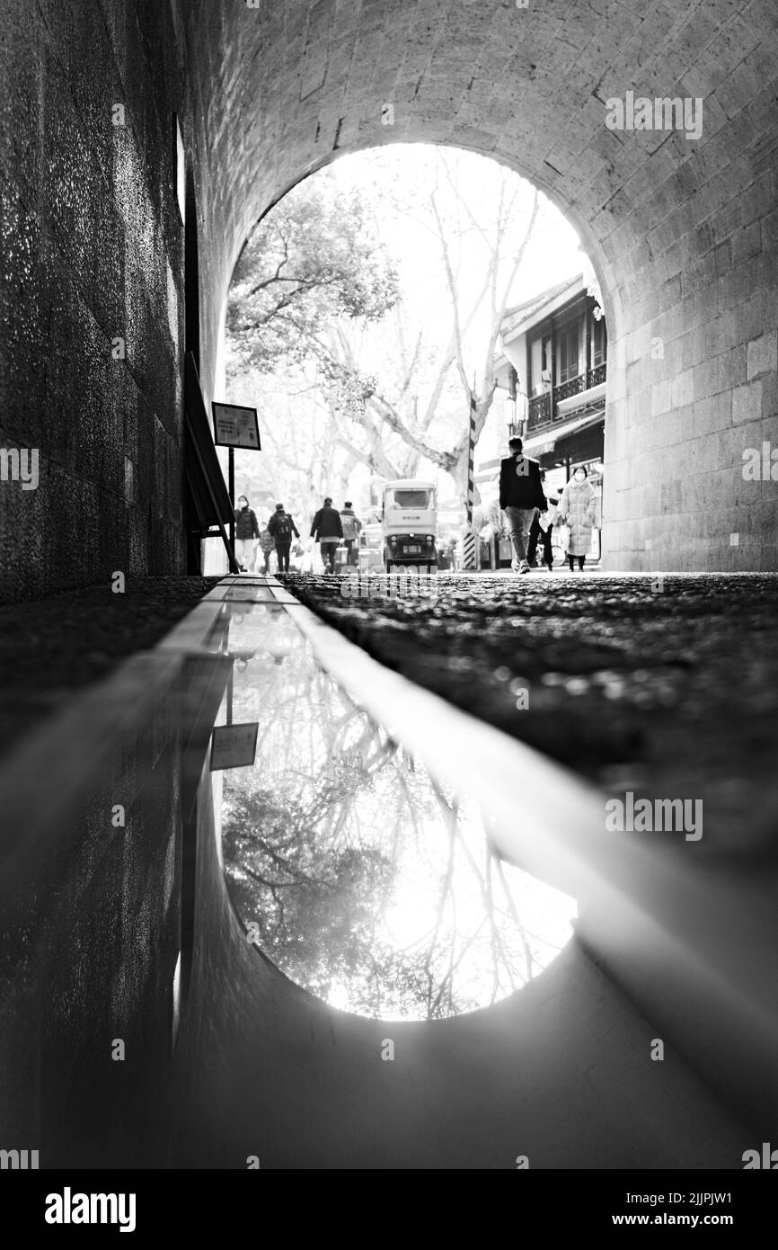 A vertical shot of people walking in the tunnel in black and white Stock Photo