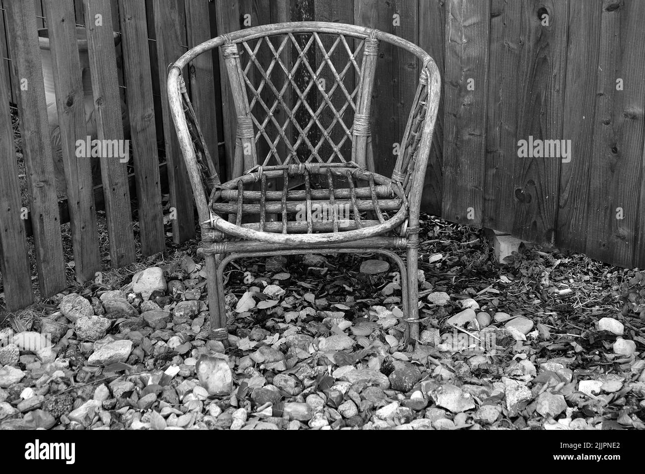 An old rattan chair displayed beside a fence Stock Photo