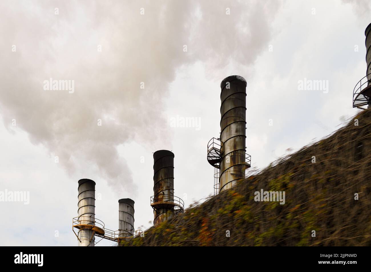 industrial smokestacks belching out smoke polluting behind a fence Stock Photo