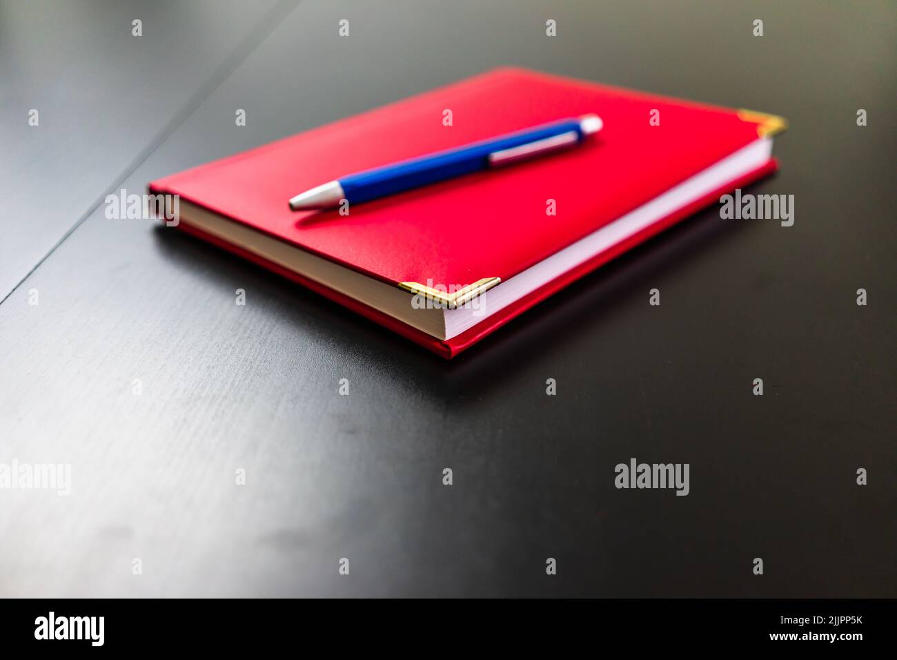 A closeup shot of a red notebook with a blue pen on a table Stock Photo