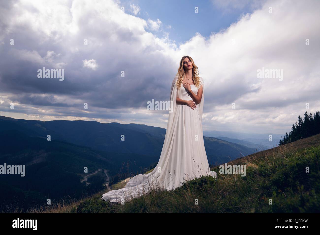 A woman in a long white wedding dress standing on the mountain Stock ...