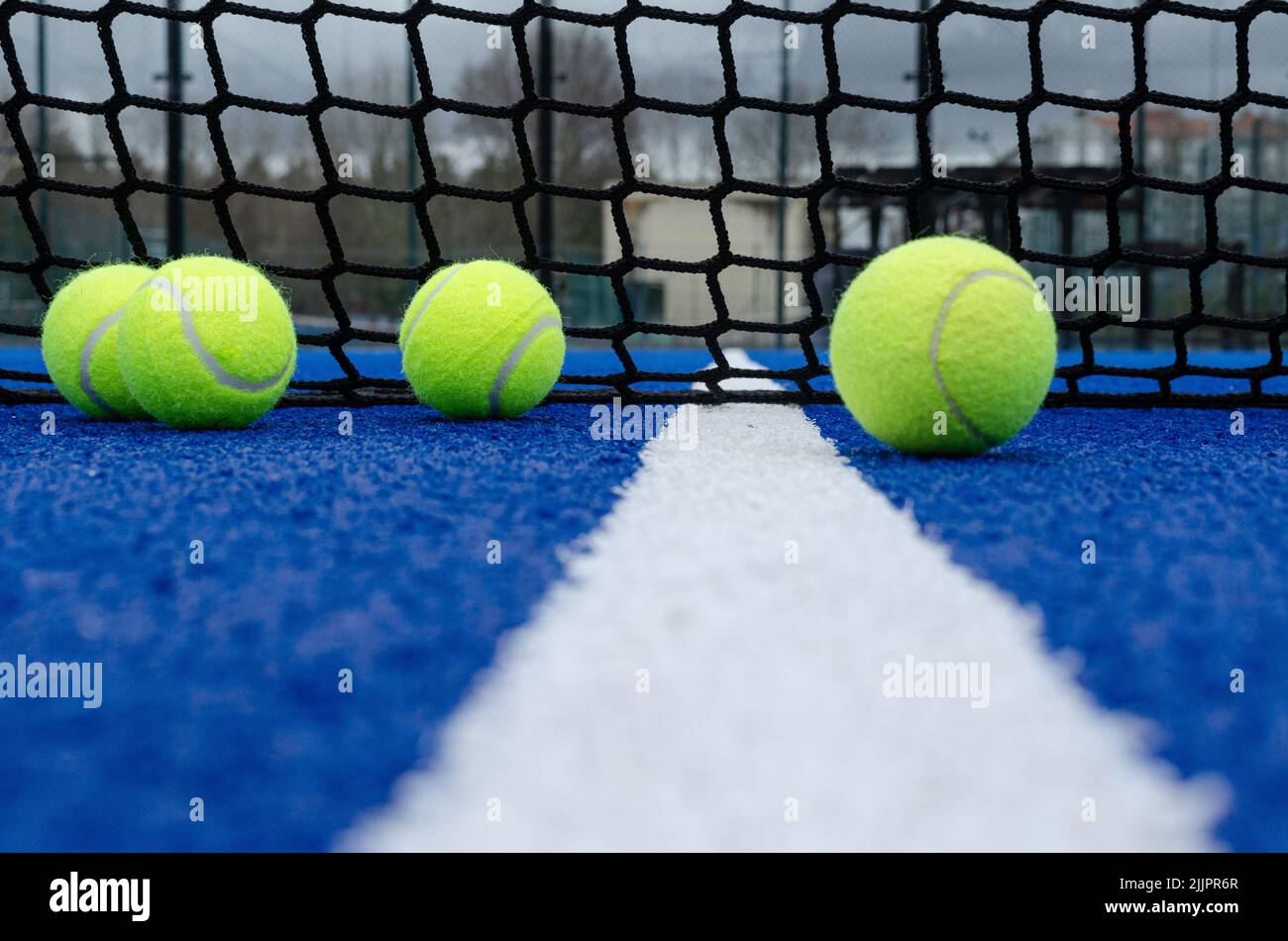 The net of a blue paddle tennis court and four balls near the white line Stock Photo