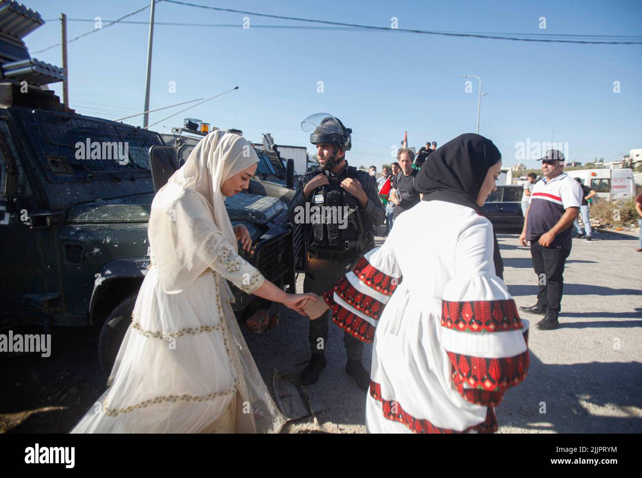 Haris Village, Palestine. 27th July, 2022. A Palestinian bride and her friend pass in front of an Israeli soldier at an Israeli checkpoint after the wedding procession was prevented at the entrance to the village of Haris in the occupied West Bank. Credit: SOPA Images Limited/Alamy Live News Stock Photo