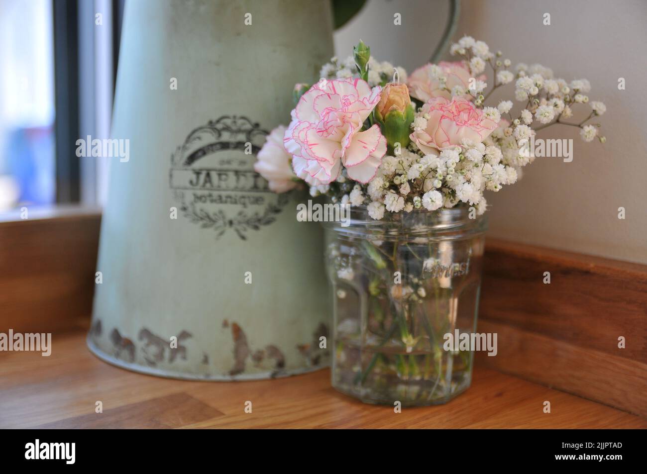 A view of beautiful pink carnation flowers in jar on a wooden surface in a cafe or an apartment Stock Photo