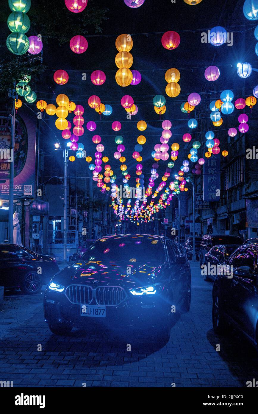 A vertical shot of a car in the street at night with colorful lights ...