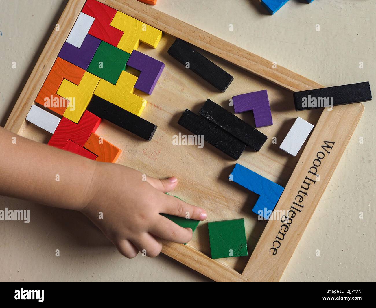 A top view of a block puzzle with colorful pieces and a child's hand playing for skills and education Stock Photo