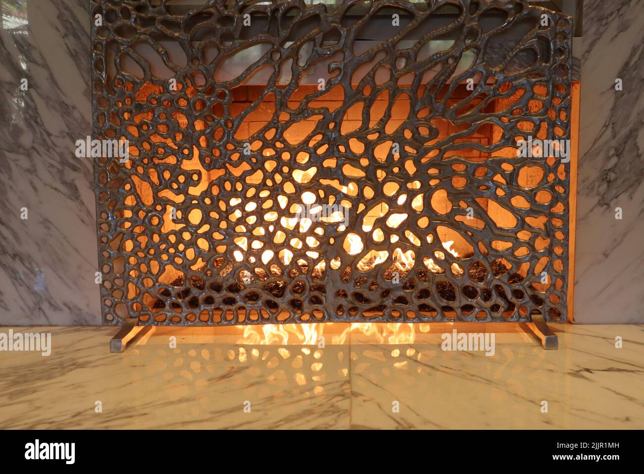 A textured fireplace cover in front of fire with marble tiling Stock Photo