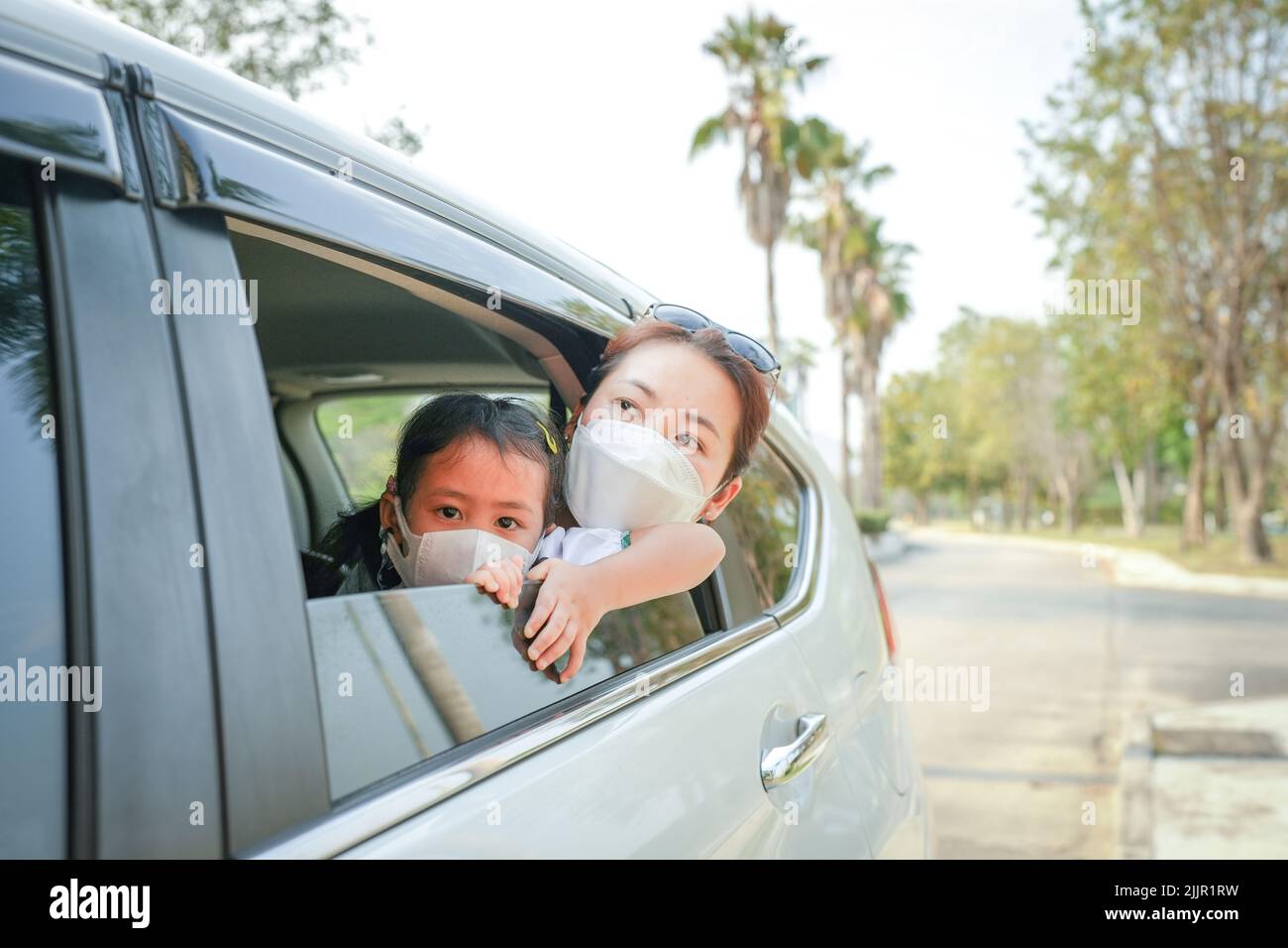 A beautiful Southeast Asian woman and her child wearing face masks looking out of the car window Stock Photo