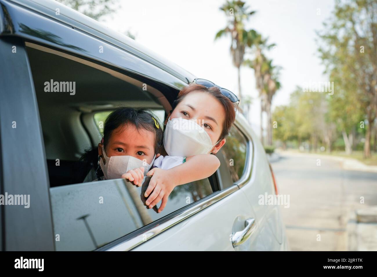 A beautiful Southeast Asian woman and her child wearing face masks looking out of the car window Stock Photo