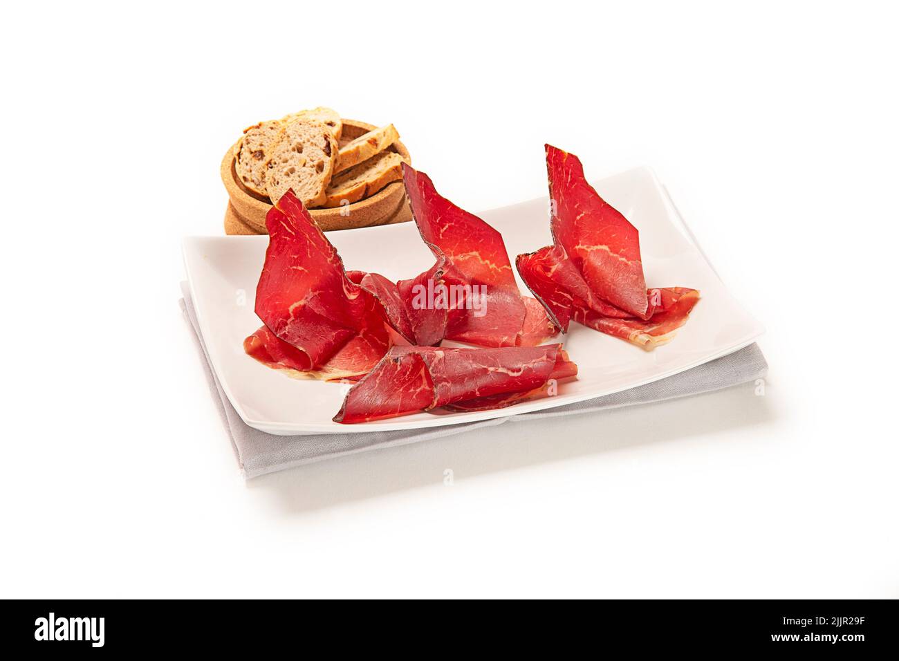 A closeup shot of bacon strips on a white platter with toasted bread in a small wooden bowl Stock Photo